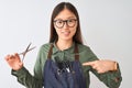 Chinese hairdresser woman wearing glasses holding scissors over isolated white background with surprise face pointing finger to Royalty Free Stock Photo