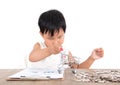 A Chinese little girl is playing with a shopping cart model on the table and there is a pile of dollar coins next to it