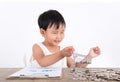 A Chinese little girl is playing with a shopping cart model on the table and there is a pile of dollar coins next to it