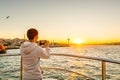 Chinese male tourist on a cruise ship taking photos of seascape at the Bosphorus strait and the sunset in Istanbul, vacation
