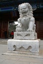 A Chinese marble stone lion sits in front of a traditional painted eave pavilion