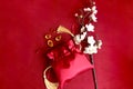 Chinese New Year, blooming plum blossom flower branch with red silk pocket money bag and gold ingot on red background, lucky item