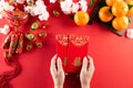 Chinese new year festival decorations. Woman hand holding pow or red packet, orange and gold ingots on a red background. Chinese Royalty Free Stock Photo