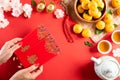 Chinese new year festival decorations. Woman hand holding pow or red packet, orange and gold ingots on a red background. Chinese Royalty Free Stock Photo