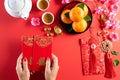 Chinese new year festival decorations. Woman hand holding pow or red packet, orange and gold ingots on a red background. Chinese Royalty Free Stock Photo