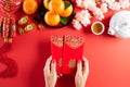 Chinese new year festival decorations. Woman hand holding pow or red packet, orange and gold ingots on a red background. Chinese Royalty Free Stock Photo