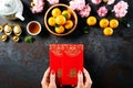 Chinese new year festival decorations. Woman hand holding pow or red packet, orange and gold ingots on a black stone background. Royalty Free Stock Photo