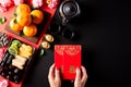 Chinese new year festival decorations. Woman hand holding pow or red packet, orange and gold ingots on a black stone background. Royalty Free Stock Photo