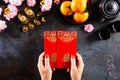 Chinese new year festival decorations. Woman hand holding pow or red packet, orange and gold ingots on a black stone texture Royalty Free Stock Photo