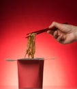 Chinese noodles in the red box. The hand pulls the chopsticks in the food on bright background Royalty Free Stock Photo