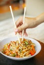 Chinese noodles with shrimps and vegetables. Person holding chopsticks with noodles over asian fried udon