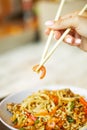 Chinese noodles with shrimps and vegetables. Person holding chopsticks with shrimp over asian fried udon