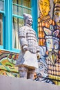 Chinese statue of man standing in front of soldier mural with bright blue windows