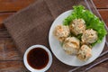 Chinese Steamed Dumpling Shumai on white dish served with soy sauce and .lettuce leaves on brown cloth and wooden table. Royalty Free Stock Photo