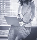 Chinese successful and satisfied businesswoman is standing with laptop computer in modern office interior near skyscraper window