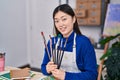 Chinese woman artist holding paintbrushes sitting on table at art studio