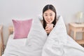 Chinese woman drinking cup of coffee covering with bedsheet at bedroom