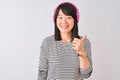 Chinese woman listening to music using pink headphones over isolated white background doing happy thumbs up gesture with hand Royalty Free Stock Photo