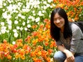 Chinese woman squatting down in front of white,orange tulips