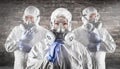 Chinese Woman and Team Behind In Hazmat Suits, Gas Masks and Goggles Against Brick Wall Royalty Free Stock Photo