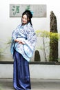 Chinese woman in traditional Blue and white Hanfu dress sit next to bonsai