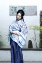 Chinese woman in traditional Blue and white Hanfu dress sit next to bonsai