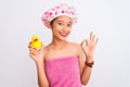 Chinese woman wearing shower towel and cap holding duck toy over isolated white background doing ok sign with fingers, excellent Royalty Free Stock Photo