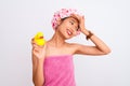 Chinese woman wearing shower towel and cap holding duck toy over isolated white background stressed with hand on head, shocked Royalty Free Stock Photo