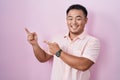 Chinese young man standing over pink background smiling and looking at the camera pointing with two hands and fingers to the side Royalty Free Stock Photo
