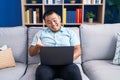 Chinese young man using computer laptop sitting on the sofa celebrating achievement with happy smile and winner expression with Royalty Free Stock Photo