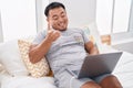 Chinese young man using laptop sitting on the bed celebrating achievement with happy smile and winner expression with raised hand Royalty Free Stock Photo