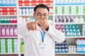 Chinese young man working at pharmacy drugstore laughing at you, pointing finger to the camera with hand over mouth, shame Royalty Free Stock Photo