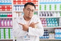 Chinese young man working at pharmacy drugstore pointing to both sides with fingers, different direction disagree Royalty Free Stock Photo