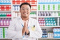 Chinese young man working at pharmacy drugstore praying with hands together asking for forgiveness smiling confident