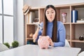 Chinese young woman holding hammer and piggy bank making fish face with mouth and squinting eyes, crazy and comical Royalty Free Stock Photo