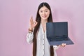 Chinese young woman holding laptop showing screen doing ok sign with fingers, smiling friendly gesturing excellent symbol Royalty Free Stock Photo