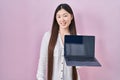 Chinese young woman holding laptop showing screen looking positive and happy standing and smiling with a confident smile showing Royalty Free Stock Photo