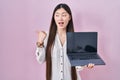 Chinese young woman holding laptop showing screen pointing thumb up to the side smiling happy with open mouth Royalty Free Stock Photo