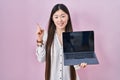 Chinese young woman holding laptop showing screen smiling happy pointing with hand and finger to the side Royalty Free Stock Photo