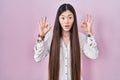Chinese young woman standing over pink background looking surprised and shocked doing ok approval symbol with fingers Royalty Free Stock Photo