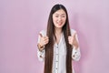 Chinese young woman standing over pink background success sign doing positive gesture with hand, thumbs up smiling and happy Royalty Free Stock Photo