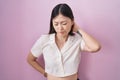 Chinese young woman standing over pink background suffering of neck ache injury, touching neck with hand, muscular pain Royalty Free Stock Photo