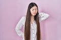 Chinese young woman standing over pink background suffering of neck ache injury, touching neck with hand, muscular pain Royalty Free Stock Photo