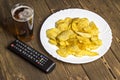 Chips with beer and TV remote control on a wooden background remote