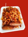 Tasty Chips masala and Sausage on a white disposable plate with orange backgound and a toothpick