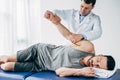 Chiropractor stretching arm of handsome patient lying on massage table Royalty Free Stock Photo