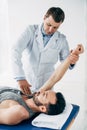 Chiropractor stretching arm of handsome patient lying on massage table with towel Royalty Free Stock Photo