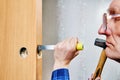 Chisel driven by hammer, cuts into wooden door frame to create mortise, with partially installed lockset hole visible in