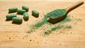 Chlorella powder in a wooden spoon and spirulina pills on a light wooden background. Nutritional supplement