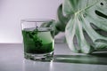 Chlorophyll extract is poured in pure water in glass against a white grey background with green leaf